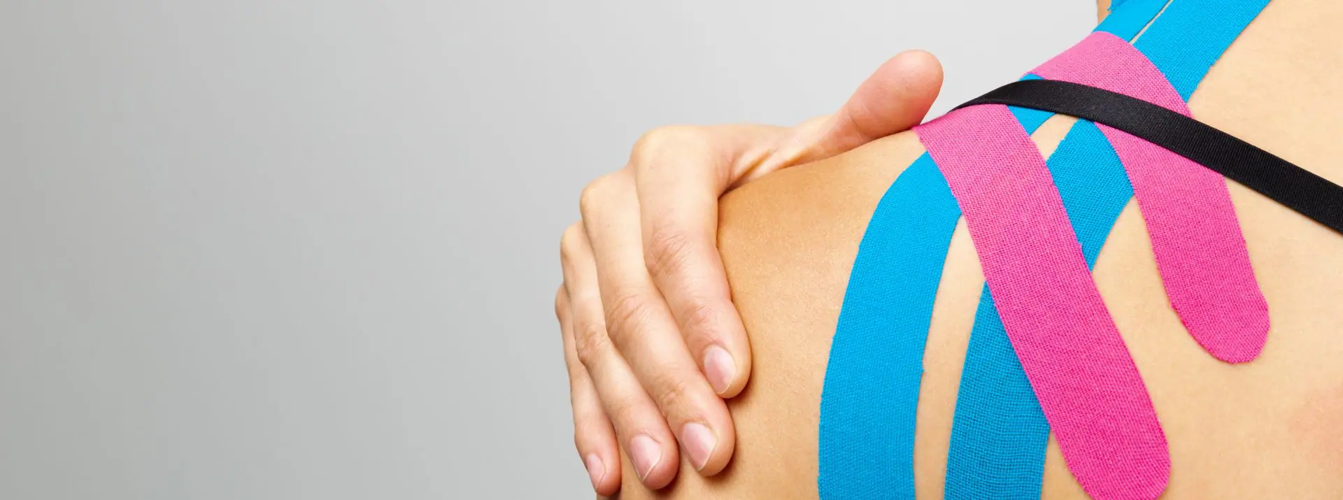 Woman with her hand on the shoulder testing the effect of Kinesio tape applied to her back by a physio